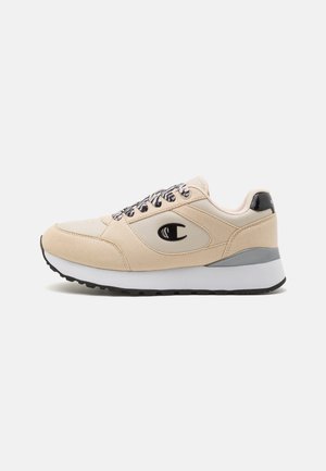 Baskets beige et crème avec lacets noirs et blancs, semelle blanche épaisse, semelle extérieure noire et logo noir sur le côté et sur la languette de talon.