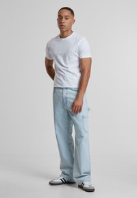 Tricou alb cu mânecă scurtă, blugi largi de culoare albastru deschis cu un buzunar pe lateral și adidași negri și albi cu dungi. Textură de țesătură netedă.