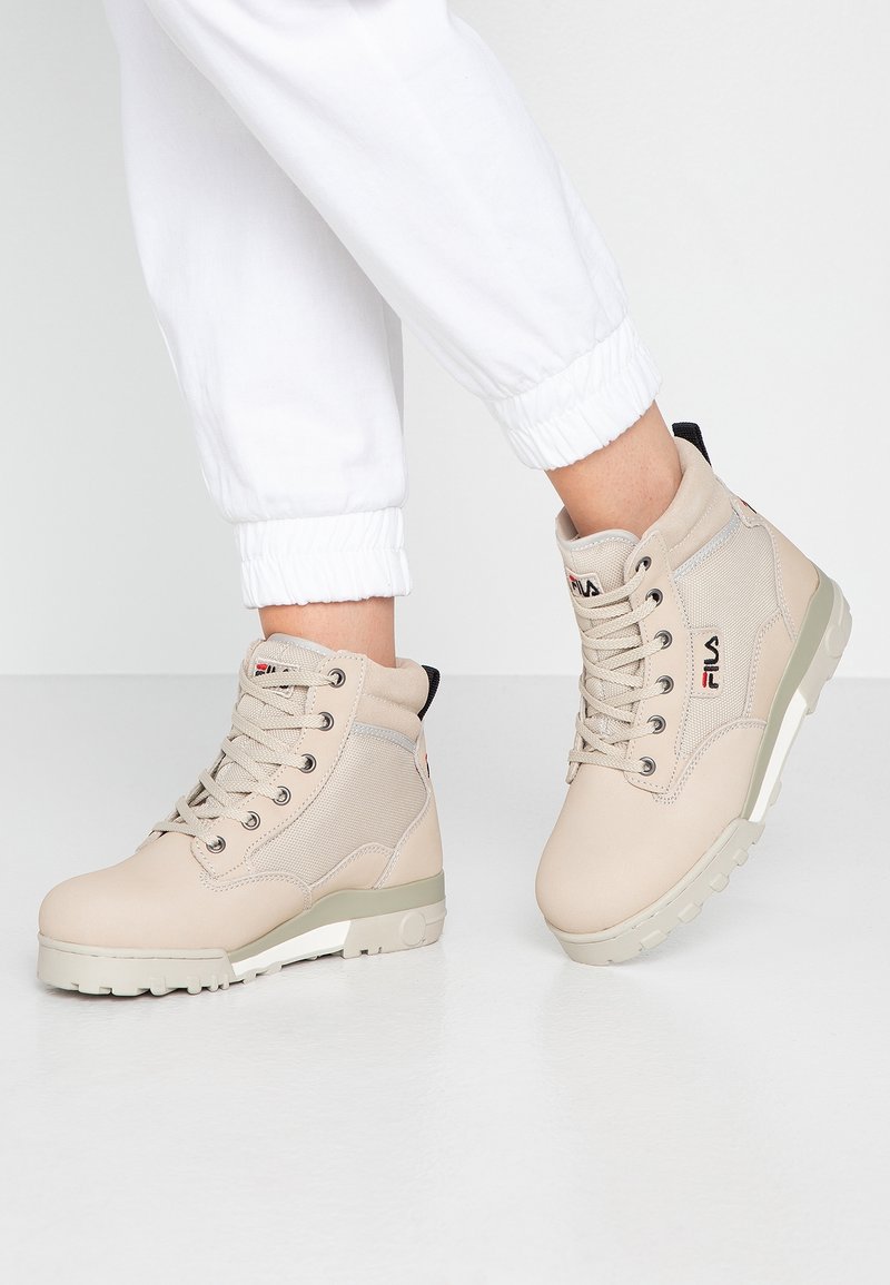 Stivali high-top beige con dettagli in rete, punta tonda, suola piatta in gomma, occhielli in metallo e logo Fila sul lato.