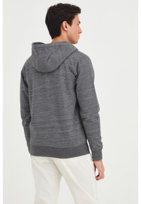 Sudadera con capucha gris hecha de tejido texturizado, que presenta un corte relajado, ribetes en el dobladillo y los puños, y un detalle de capucha notable.