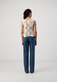 Haut en crème à mailles en dentelle avec une coupe décontractée, présentant un motif floral et un large col, associé à un jean bleu taille haute.