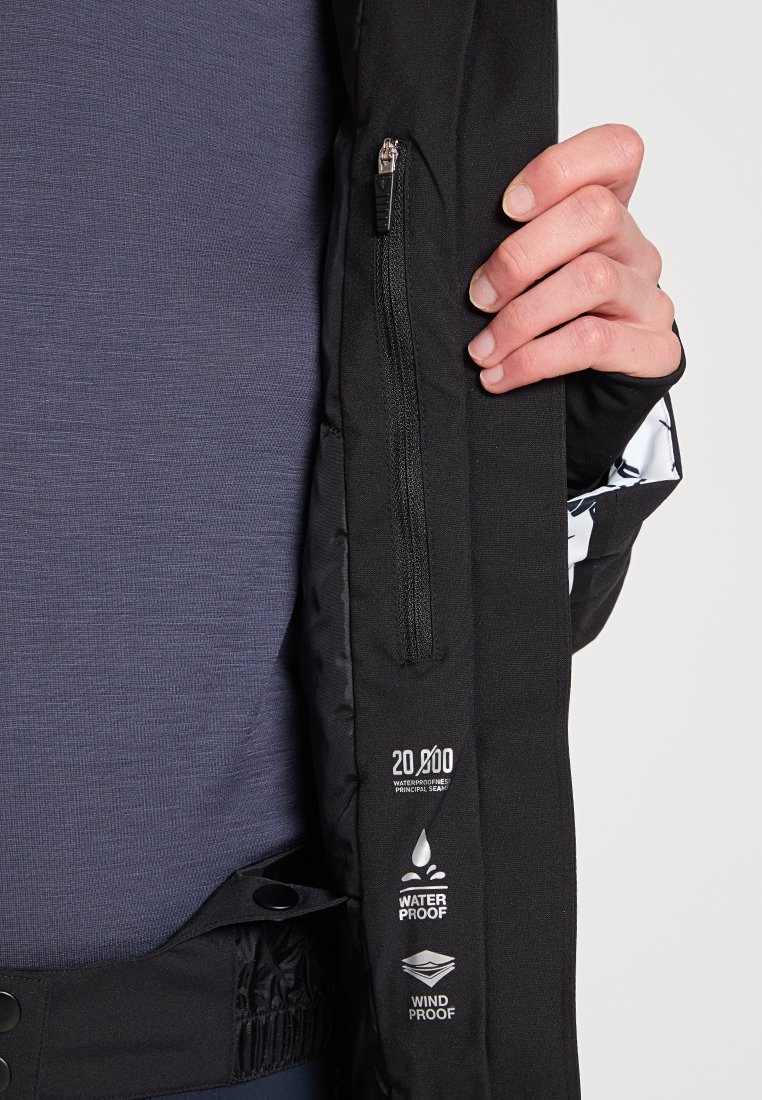 Czarna wodoodporna kurtka z zamkiem błyskawicznym i kieszenią, z ikonami wodoodporności i wiatroszczelności, połączona z teksturowaną granatową bluzką pod spód.