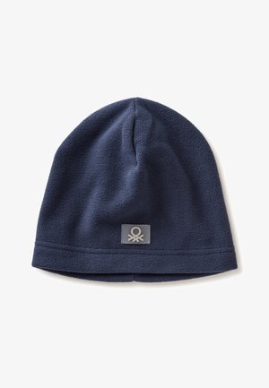 Námořnická modrá fleecová čepice, zaobleného tvaru s lemovaným okrajem. Obsahuje malou čtvercovou nálepku s abstraktním vzorem našitou na boku.