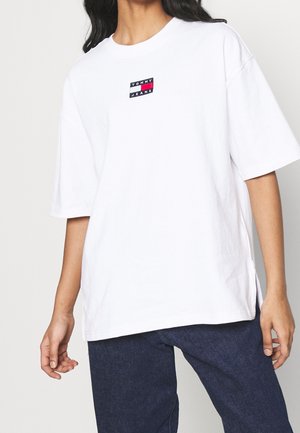 Weißes Baumwoll-T-Shirt mit kleinem schwarzen, roten und blauen "Tommy Jeans"-Logo auf der Brust. Lässiger Schnitt mit kurzen Ärmeln und Seitenschlitzen.