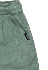 Gröna corduroybyxor med en texturerad yta, elastisk midja, sidofickor och en liten svart logg på vänster sida.