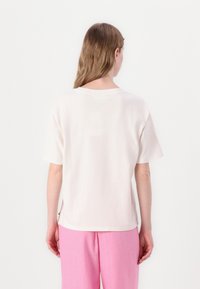 Lichtbeige katoenen T-shirt met korte mouwen, ronde hals en zijsplitten. Basisontwerp, gladde textuur, van achteren weergegeven.