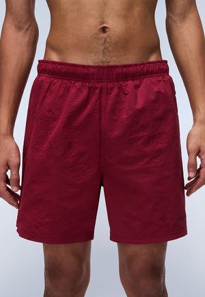 Burgunderfarbene Badehose aus strukturiertem Stoff mit elastischem Bund und mittellangem Schnitt, der schlichte Muster aufweist und keine sichtbaren Beschläge hat.