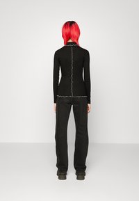 Svart långärmad topp med en rynkad vit kant längs halsringningen och nederkanten; ihop med svarta raka byxor och klumpiga stövlar.