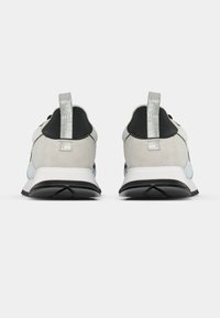 Ténis com esquema de cores cinzento e preto, materiais em camurça e sintético, com um puxador de calcanhar texturizado e sola de borracha lisa.