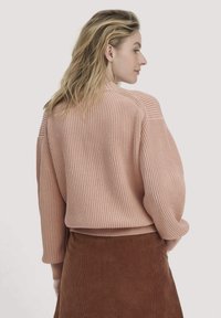 Rosa gerippter Pullover mit langen Ärmeln, rundem Ausschnitt und lässiger Passform, kombiniert mit einem braunen Cordrock.