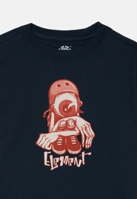 T-shirt en coton bleu marine avec un design graphique rouge d'une figure tenant des baskets, avec le mot "Element" en texte stylisé en dessous.