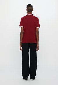 Burgunderfarget polo-shirt med hvit kant ved kragen og ermene, kombinert med løse svarte bukser. Stoffet ser glatt og lett ut.