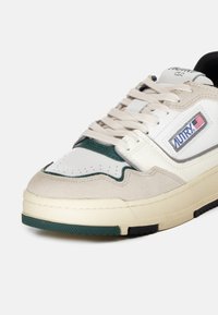 Sneaker bianco con accenti verdi e beige, realizzato in pelle e suede, caratterizzato da punta perforata, design con lacci e logo del brand.