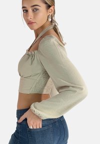 Hellbeiges, kurzes Oberteil mit Puffärmeln, strukturiertem Stoff und quadratischem Ausschnitt. Kombiniert mit dunkelblauen, hoch taillierten Jeans.