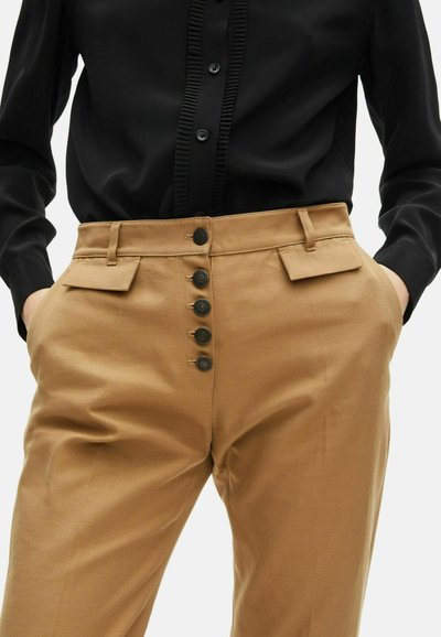 Beige op maat gemaakte broek met een rechte pijp, voorzien van een hoge tailleband, vijf zwarte knopen en zijzakken. Glad stoftextuur.