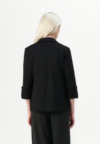 Svart blazer med trekvartslanger, skreddersydd passform, brettede mansjetter, glatt tekstur, med et enkelt design uten dekorasjoner.