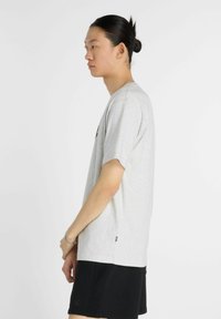 Camiseta de algodón gris con mangas cortas, ajuste relajado y cuello redondo, exhibida junto a pantalones cortos negro. Presenta un logotipo de marca sutil.