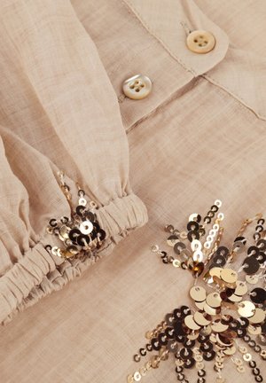 Beige long-sleeve blouse with pearl buttons and gold sequins embroidered near gathered elastic cuffs and on the fabric.