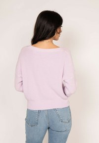 Pull en tricot côtelé mauve clair avec un large col et une coupe décontractée, associé à un jean en denim bleu taille haute.