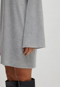 Graues geripptes Kleid mit langen Ärmeln, das eine lockere Passform und eine weiche Textur bietet. Sichtbare Nähte und ein lockerer Saum runden das Design ab.