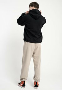 Czarna bluza z kapturem, beżowe dresy i czarne trampki z pomarańczowymi akcentami. Prosty design, luźny krój, gładka tekstura materiału.