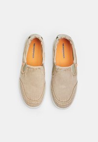 Buty wsuwane z brązowego materiału, z elastycznymi akcentami, białymi podeszwami i pomarańczowymi wkładkami. Gładka tekstura bez widocznych wzorów.