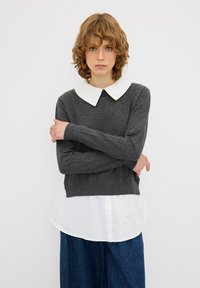 Grauer Pullover mit weißem Kragen, langen Ärmeln und einem cropped Design, über einem weißen Hemd getragen. Sanfte Textur und lässige Passform.