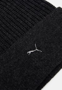 Gorro de punto negro con textura acanalada, que presenta un acento del logo plateado de Puma en el lateral. Material suave y cálido.