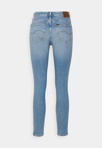 Jeans skinny de color azul claro con una textura de denim suave. Presenta un parche de marca de cuero marrón y dos bolsillos traseros con costuras curvadas.