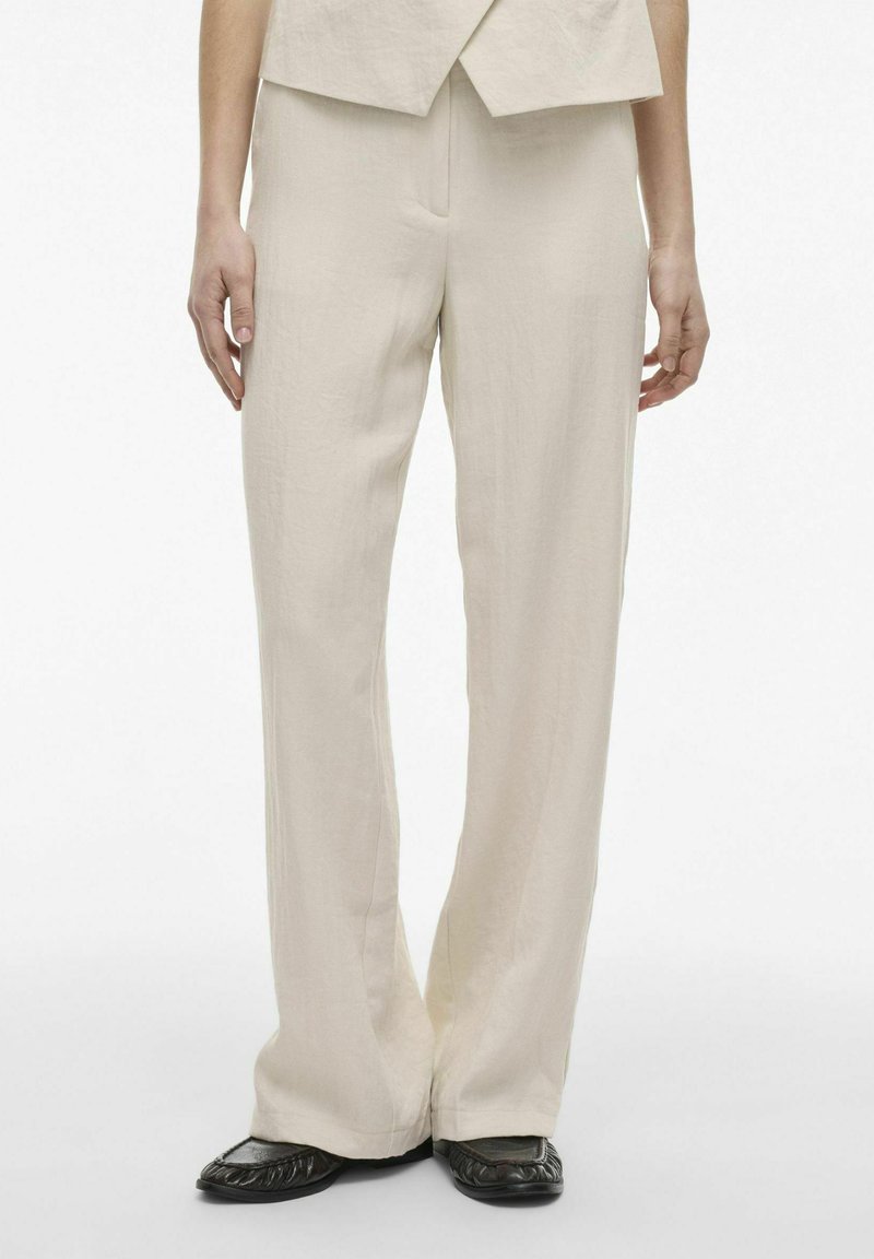 Beige, wijde pantalons gemaakt van lichtgewicht stof met een gladde textuur. In combinatie met zwarte schoenen met een subtiele, geplooide afwerking bij de taille.