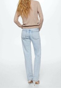 Hellblaue Jeans mit geradem Bein, ausgestattet mit Gesäßtaschen und einem verblassten Finish, kombiniert mit einem beigen Pullover und hellen Sandalen.