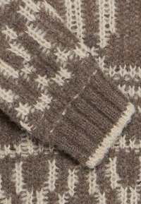 Strickpullover-Detail mit einem braun- und cremefarbenen Muster, gerippten Bündchen, strukturiertem Wollmaterial und einer weichen Oberflächenstruktur.