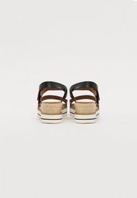 Sandales en cuir noir avec deux brides, présentant un talon de style espadrille tressé et une semelle rayée blanche, vues de l'arrière.