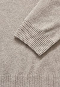 Beige Strickpullover mit gerippten Bündchen und Saum, der eine weiche Textur und ein einfaches Design aufweist. Keine Muster oder zusätzlichen Details sichtbar.