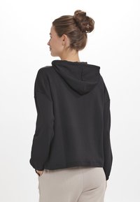 Svart huvtröja med en avslappnad passform, något kortare längd och långa ärmar. Slät tyg med en subtil lyster och utan mönster.