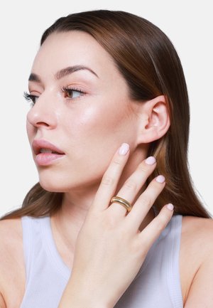 Anello a spirale color oro sulla mano del modello, con una finitura testurizzata e una forma liscia e arrotondata. La pelle ha un naturale splendore.