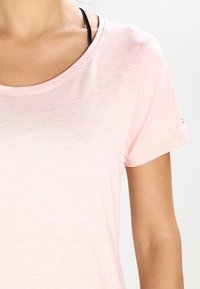 Camiseta de manga corta rosa claro con una textura suave y lisa y un escote redondo. Cuenta con un acento negro en la manga izquierda.