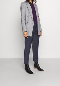 Blazer à carreaux gris clair sur un haut violet, associé à un pantalon tapered navy et des bottines noires à petit talon.