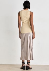 Beige ribbad tanktop kombinerad med en lång, glänsande, ljusrosa satinkjol och svarta klacksandaler, sedd bakifrån.