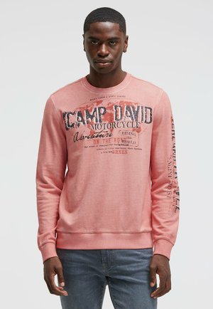 Pink sweatshirt with long sleeves, round neck, and front graphics. Text includes "CAMP DAVID" and "MOTORCYCLE." Soft, casual fabric.