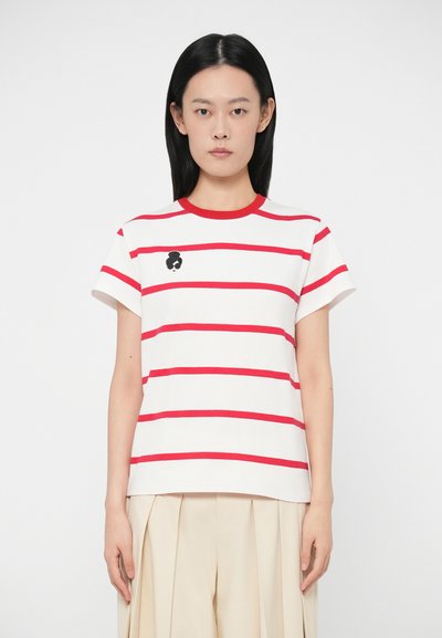 T-shirt bianca con righe orizzontali rosse e colletto rotondo. Include un piccolo dettaglio grafico nero sul petto. Materiale in cotone.