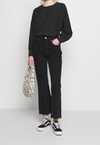 Svart långärmad topp med plisserade detaljer, kombinerad med högmidjade svarta jeans med trasiga sömmar. Svart-vita sneakers och en mönstrad väska.