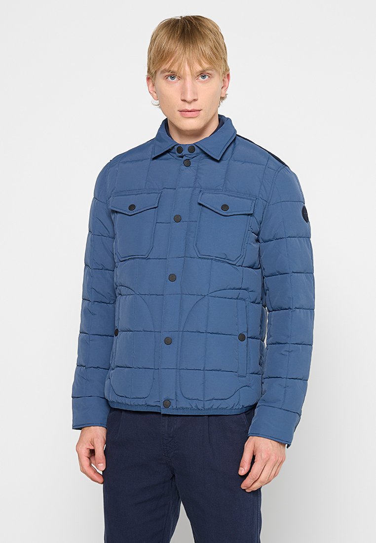 Giacca imbottita blu, con chiusura a bottoni, due tasche sul petto, design trapuntato e dettagli neri sulle spalle.