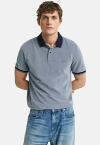 Lichtblauwe polo gemaakt van gestructureerde stof, met een marineblauwe kraag met witte strepen en een klein logo op de borst.