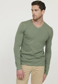 T-shirt vert à manches longues avec un col en V, en coton doux, présentant un petit logo sur la poitrine et un design ajusté.