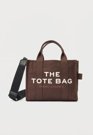 Bruine rechthoekige tote bag met korte handvatten, zwarte verstelbare schouderriem en witte tekst "THE TOTE BAG MARC JACOBS" aan de voorkant.