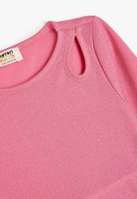 Rosa Kinderoberteil mit glatter, glitzernder Textur. Verfügt über einen runden Ausschnitt und ein Schlüssellochdetail an der Schulter. Baumwollmischgewebe.