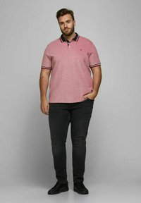 Rode heider polo shirt met een marineblauwe kraag en strepenaccenten. Draagt met een donkere jeans en zwarte schoenen; korte mouwen, ontspannen pasvorm.
