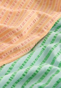 Zachte stof met roze en oranje strepen die over een lichtblauwe stof met groene strepen overlappen, beide tonen zachte plooien en textuur.