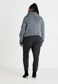 Suéter gris de punto con un cuello alto, combinado con pantalones gris oscuro. La modelo lleva botas de tacón alto de ante negras.